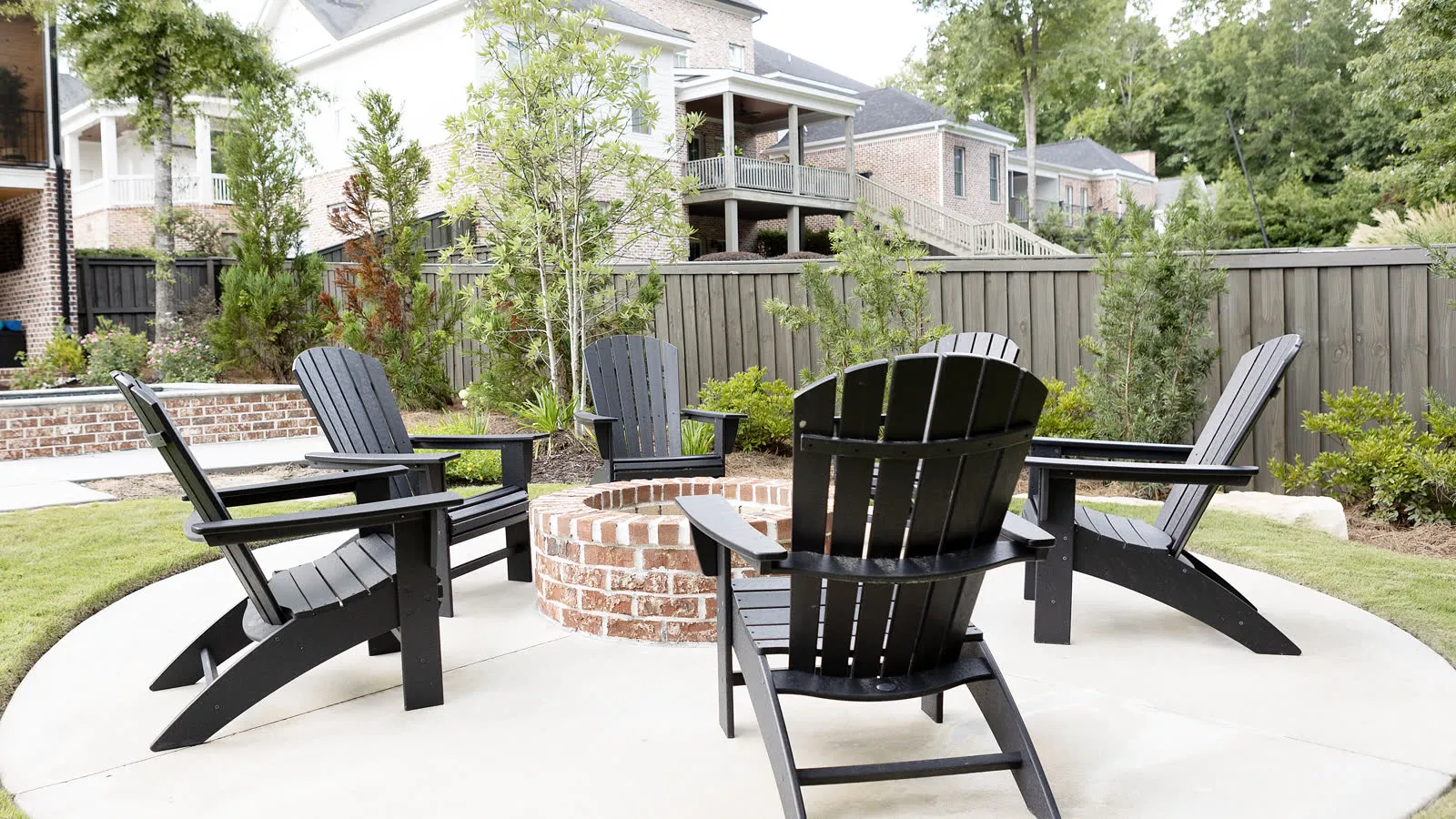 Brick fire pit ringed by black Adirondack chairs on a circular concrete patio