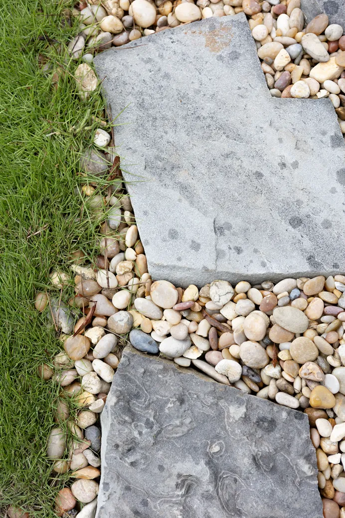 Bluestone stepping stones set into a bed of river rock beside mown turf