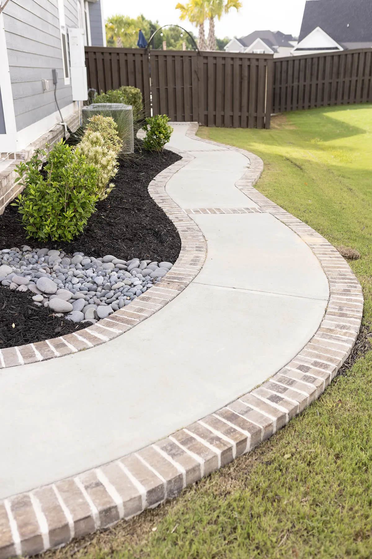 Curved planting bed with fresh mulch and river rock along a brick-edged walk