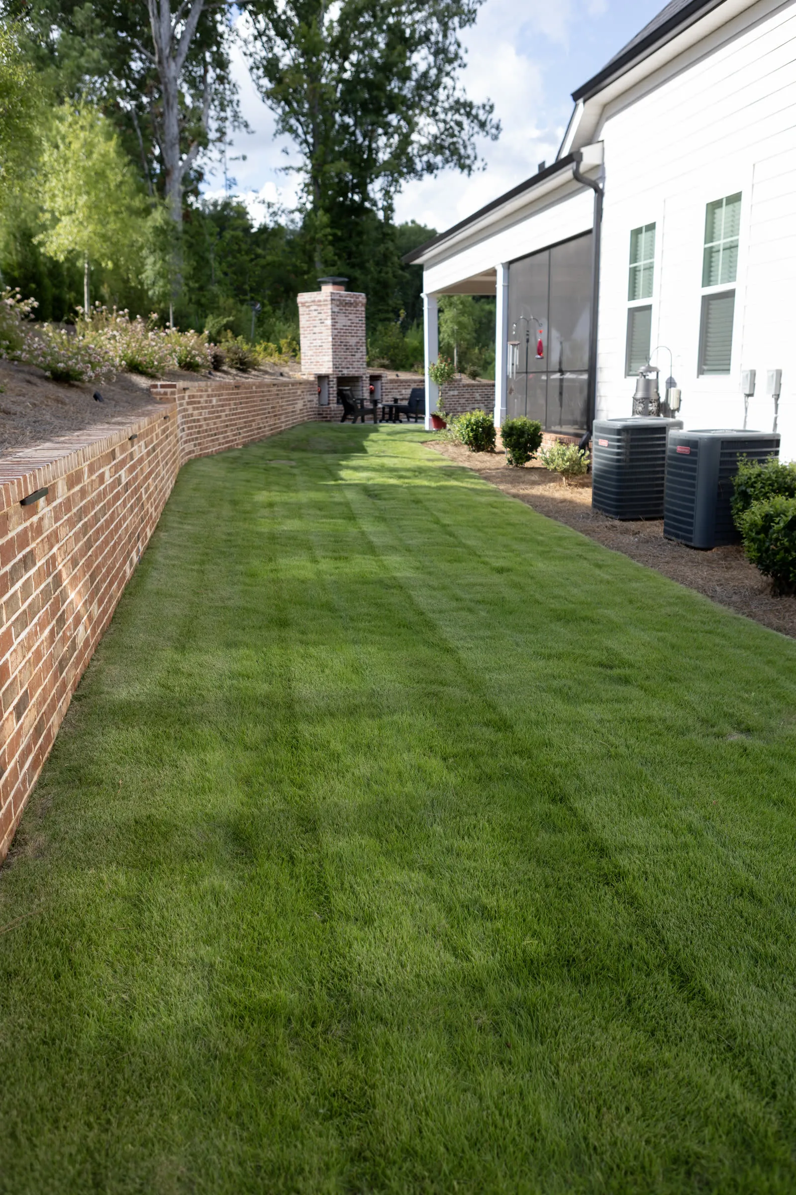 Freshly laid, striped sod running along a brick garden wall