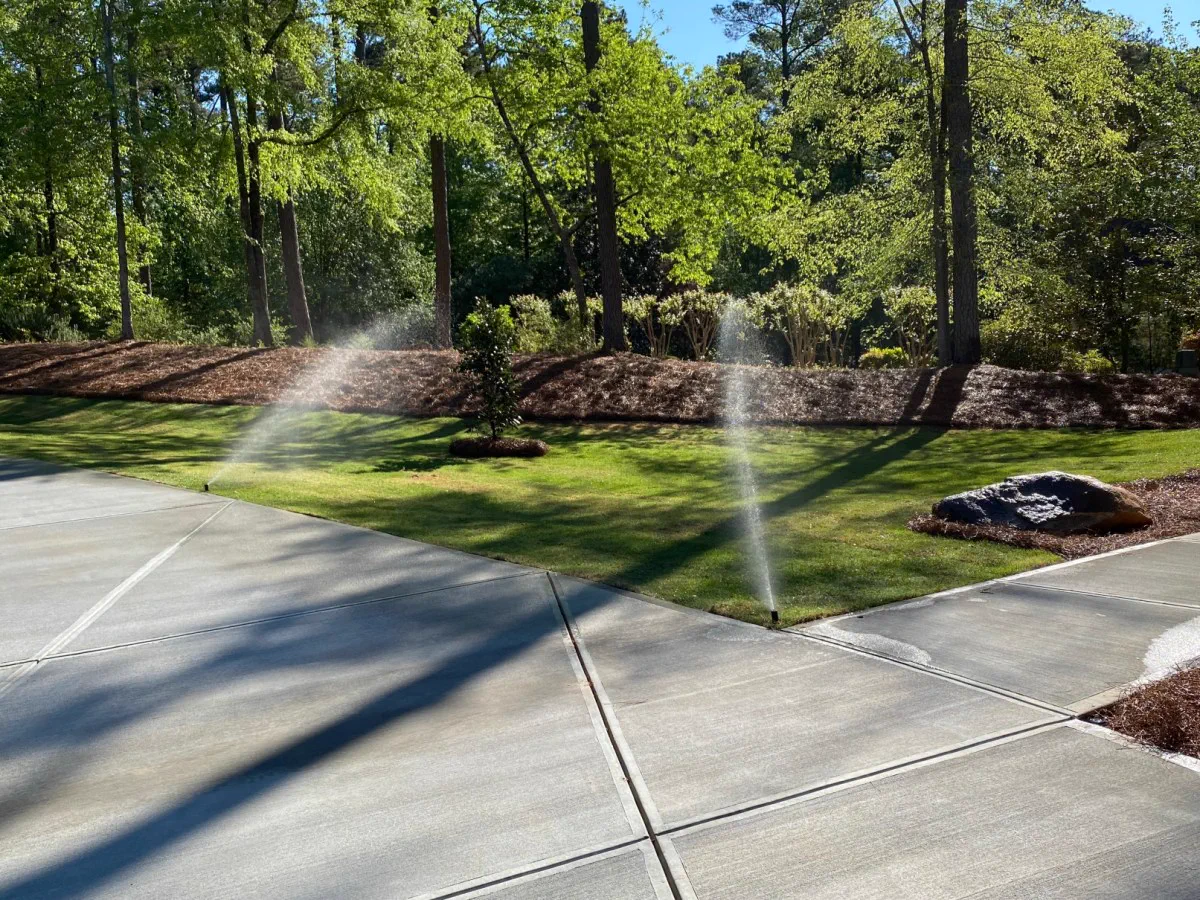Sprinklers watering a mown lawn beside a driveway