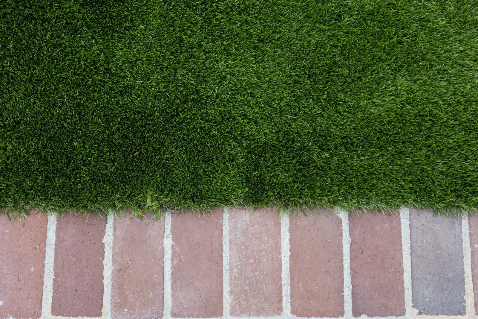 Mown turf meeting a brick paver edge, cut clean along the joint